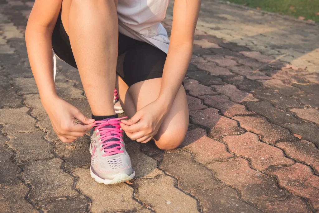 Runner tying shoes before restarting running on a park path